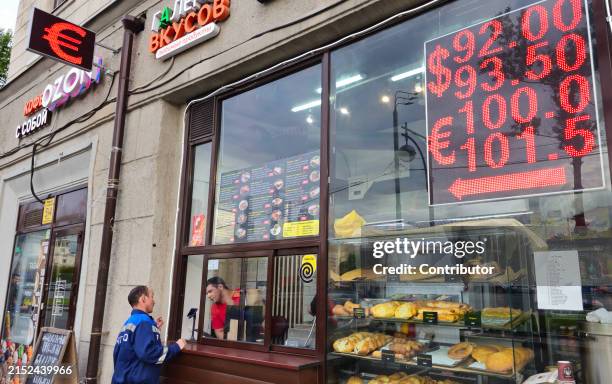 Man purchases a shawarma at a street cafe as an electronic panel of an exchange office with exchange rates for the U.S. Dollar and Euro to Ruble is...
