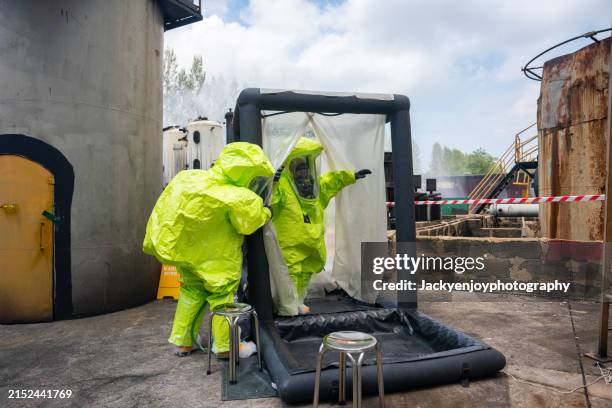 spend time in an inflatable shower tent being cleaned. it shows dedicated workers in protective gear going through an inflatable shower tent with disinfectant and wiping chemical residue off their suits. - mono blanco traje protector fotografías e imágenes de stock