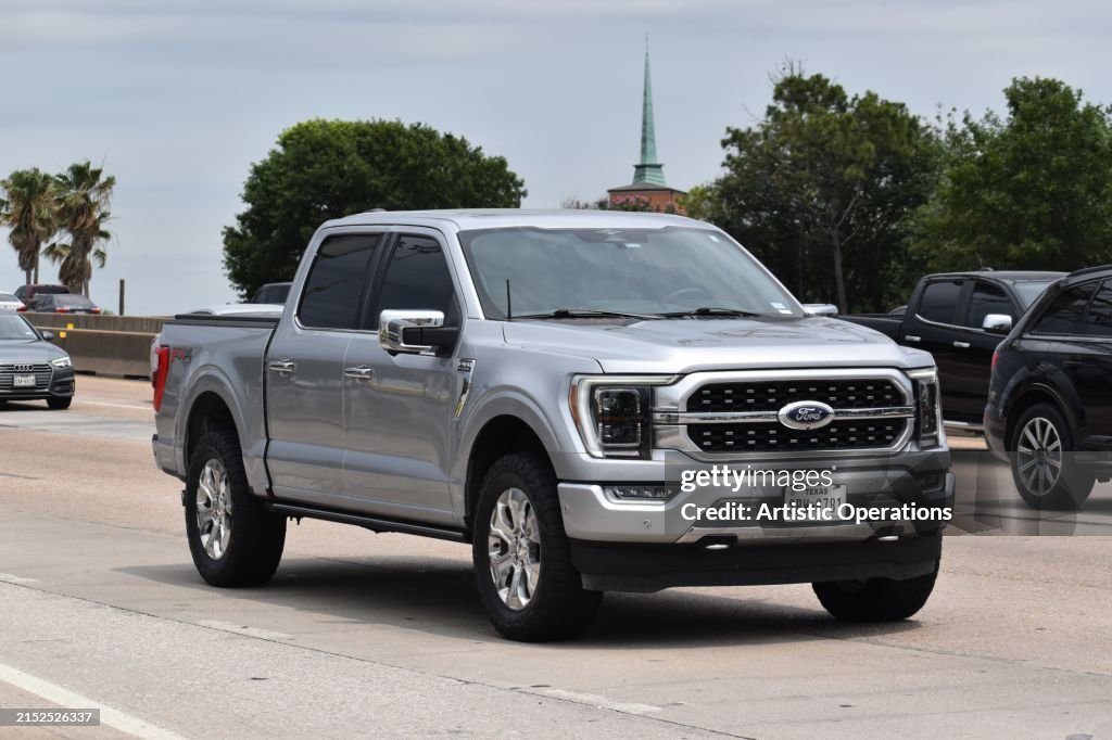 A portrait of a gray Ford F-150 pick-up truck traveling down a highway in moderate traffic