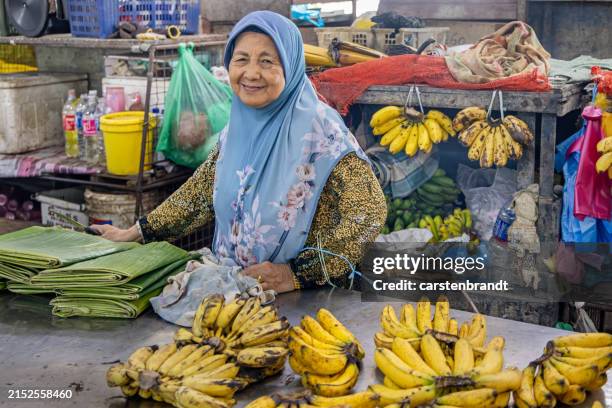 happy female greengrocer at a market stall selling bananas - bazaar stockfoto's en -beelden