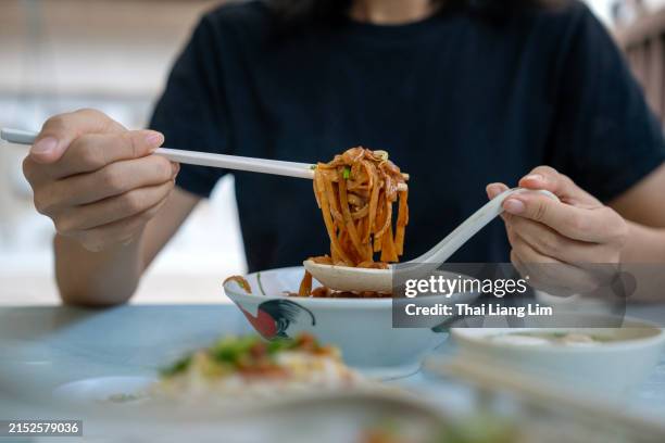 cropped shot of an asian woman enjoying flat rice noodles withe duck meat and fish ball, popular street food in penang, malaysia. - eating rice noodles stock pictures, royalty-free photos & images