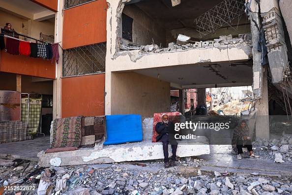 Devastated Building Displaced Palestinians sit in front of a devastated building in Khan ...
