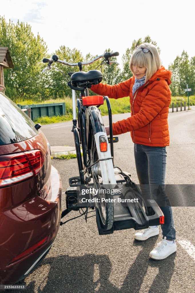 Senior woman unloading her bicycle from a car bike rack