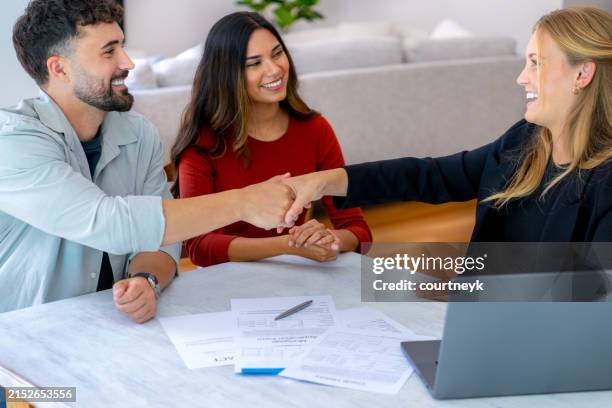 real estate or insurance agent or lawyer shaking hands with couple. they are signing home loan mortgage or contract documents. - home loan australia stock pictures, royalty-free photos & images