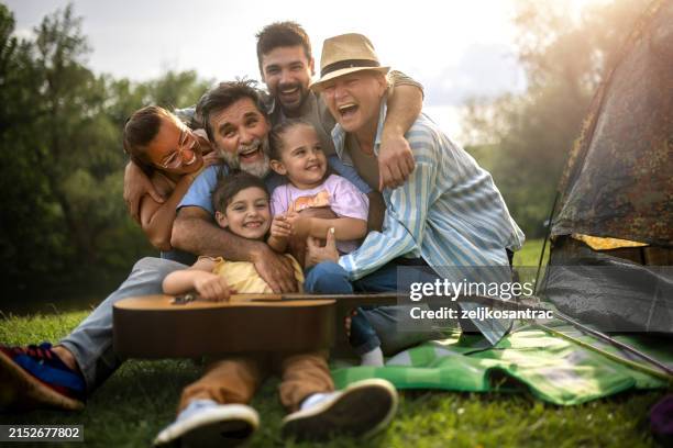 multigenerational family camping in nature and singing, playing the guitar next to the tent - grandpa son stock pictures, royalty-free photos & images