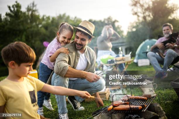 a multigenerational family is camping in nature and they make barbeque - bbq stockfoto's en -beelden