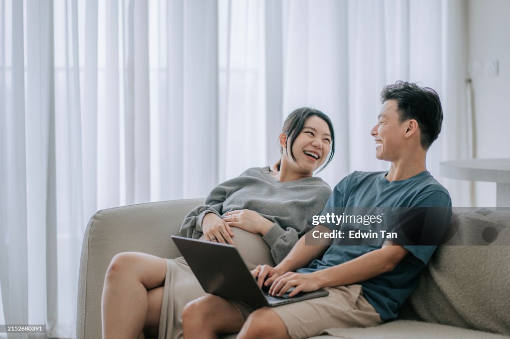 Asian Chinese pregnant woman enjoy bonding time with her husband in living room using laptop