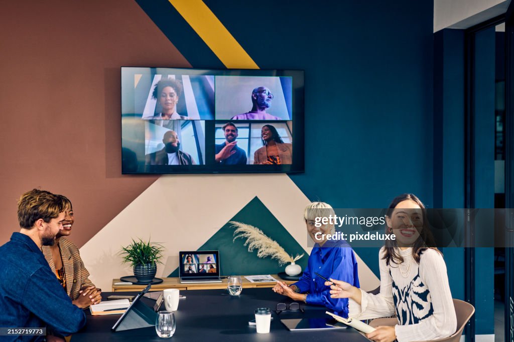 Team members in a modern office engaging with remote colleagues via a video conference call. Hybrid work environment and digital communication concept