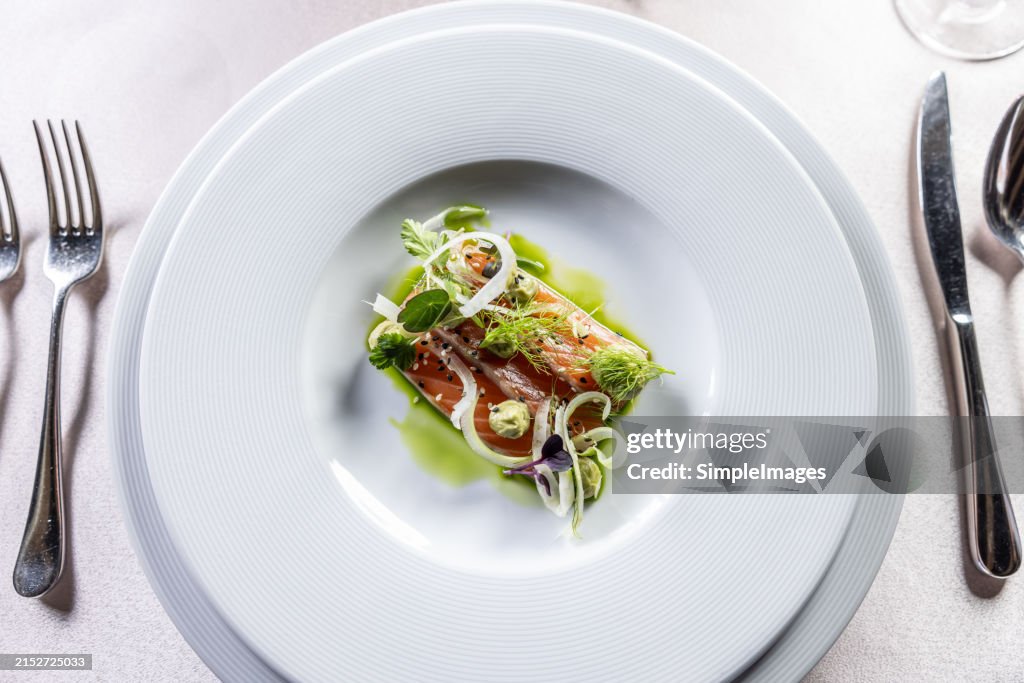 Marinated salmon with avocado, cilantro, lemon and sesame, Creatively prepared appetizer on a white plate in a restaurant.
