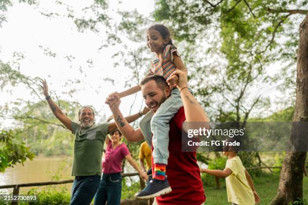patrigno che si diverte durante il piggyback con la figlia adottiva in un parco pubblico - parco naturale foto e immagini stock