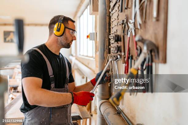 young male carpenter choosing a tool in his workshop - tool rack stock pictures, royalty-free photos & images