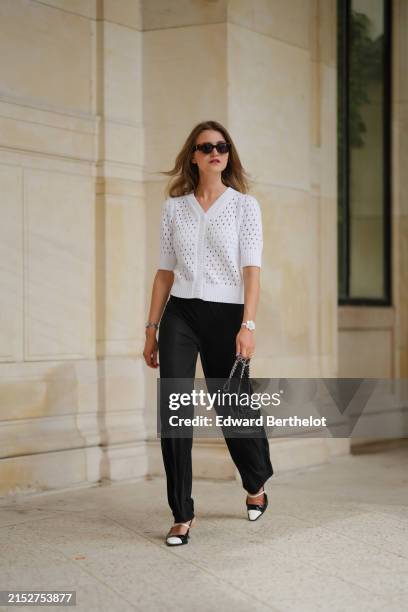 Segolene Hyppolite wears sunglasses, a white wool cardigan / top from Agnes B, a white flower shaped bracelet, a Chanel bag with floral texture /...
