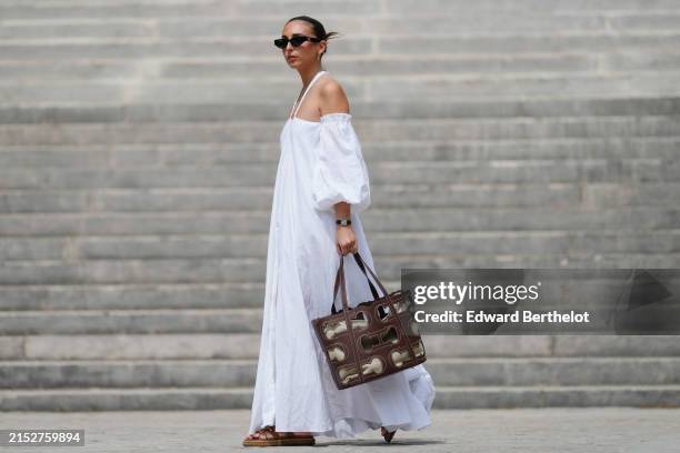 Gabriella Berdugo wears sunglasses, earrings, a white off-shoulder linen gathered dress from kalita with balloons / puff sleeves, a brown summer bag...
