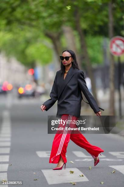 Emilie Joseph wears sunglasses, earrings, red lipstick, a black oversized / structured virgin wool blend Blazer with lapel-collar by Victoria Beckham...