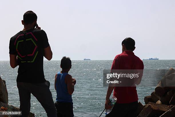 Palestinian youths stand on a jetty in Gaza City with a view of navy vessels off the coast as part of a humanitarian "maritime corridor" announced by...