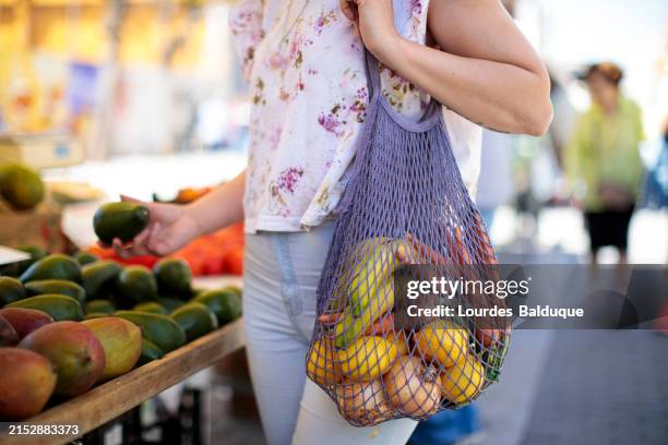 woman buys fruit and vegetables at the street market with ecological bag - greengrocers shop stock pictures, royalty-free photos & images