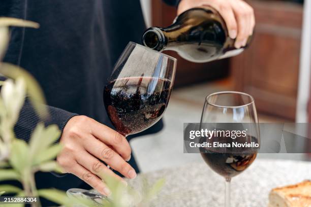 female hands pour red sparkling wine from a bottle into a glass, for an aperitif on the terrace - vinho tinto imagens e fotografias de stock