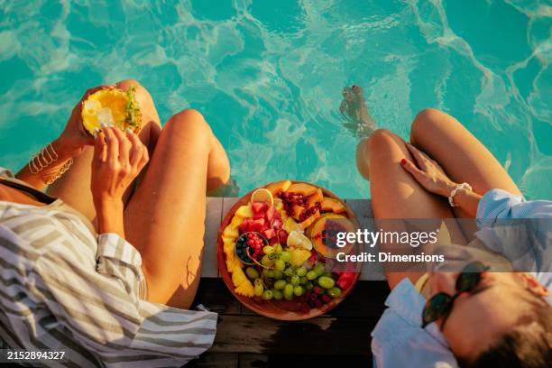 two friends eating fruits by the pool - tropical fruit stock pictures, royalty-free photos & images