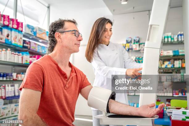 farmacéutica midiendo la presión arterial del hombre en la farmacia - instrumento de medida fotografías e imágenes de stock