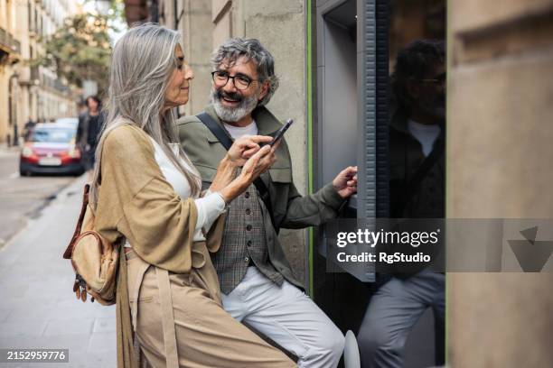 mature couple taking the money on the atm - couple at atm stock pictures, royalty-free photos & images