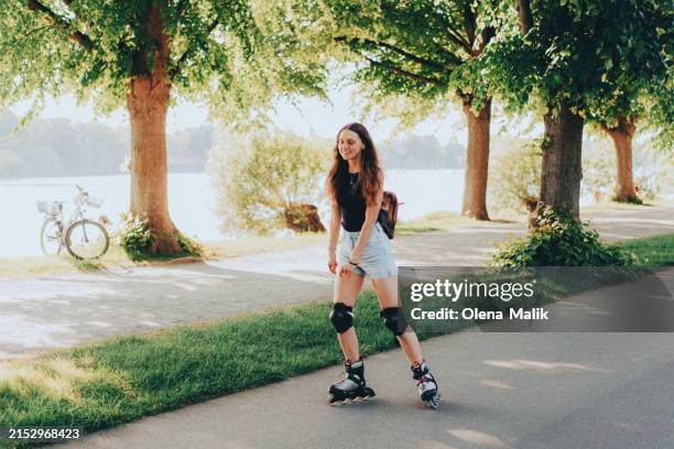 young happy woman roller skating during spring day in the park - skaten stockfoto's en -beelden