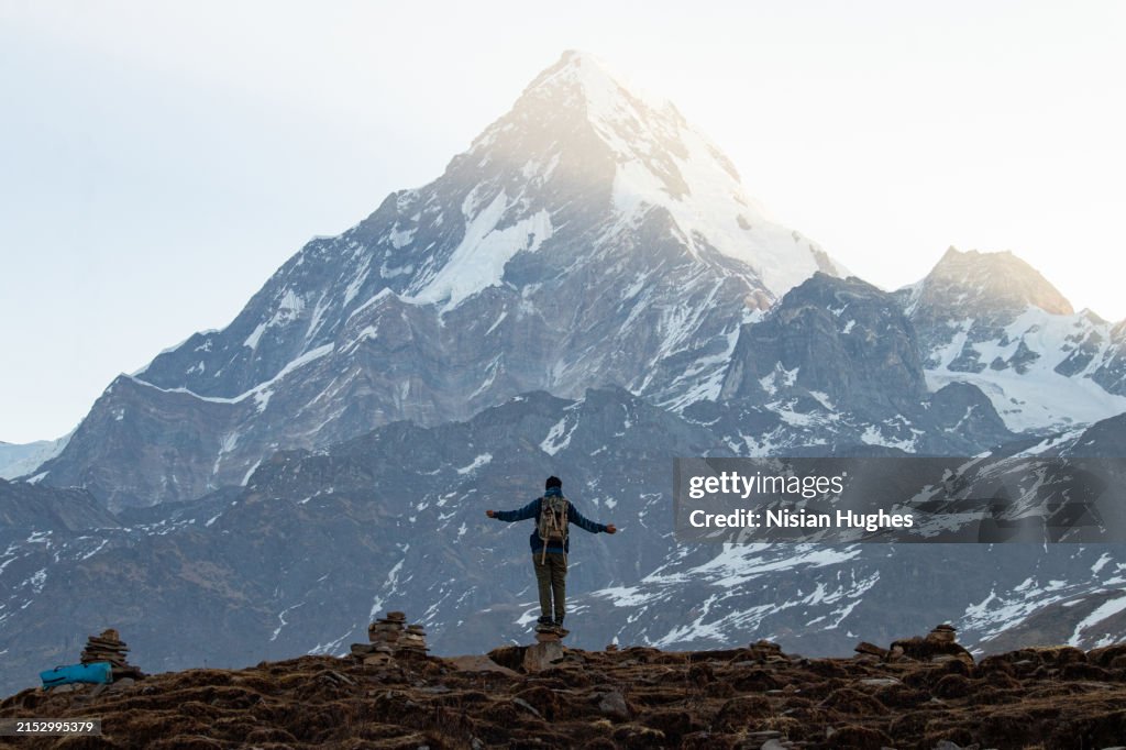 Man standing on a mountain in Nepal with arms outstretched, morning daylight