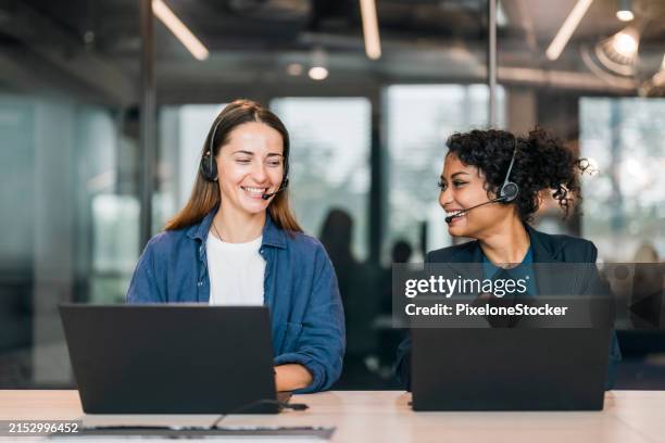 cheerful young female customer service representative working by colleague at desk in call center. - kommunikationsberuf stock-fotos und bilder