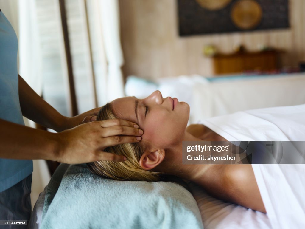 Relaxed woman receiving head massage at the spa.