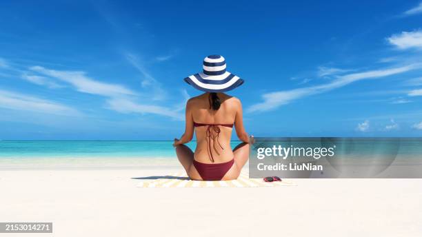 young attractive woman in bikini practicing yoga meditation on the exotic beach - mature women in swimwear hats and sunglasses on beach stock pictures, royalty-free photos & images