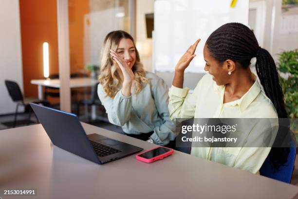 happy young female colleagues cheering in office - high five stockfoto's en -beelden