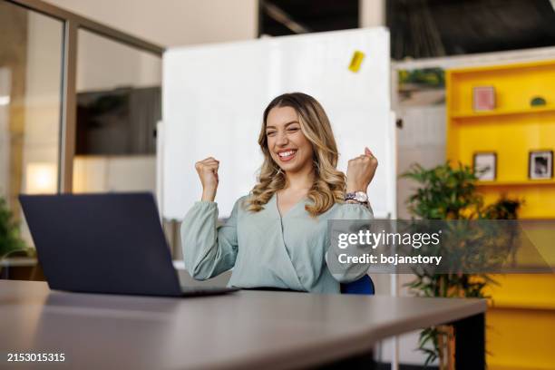excited businesswoman triumphing with fist up in office - jubeln stock-fotos und bilder