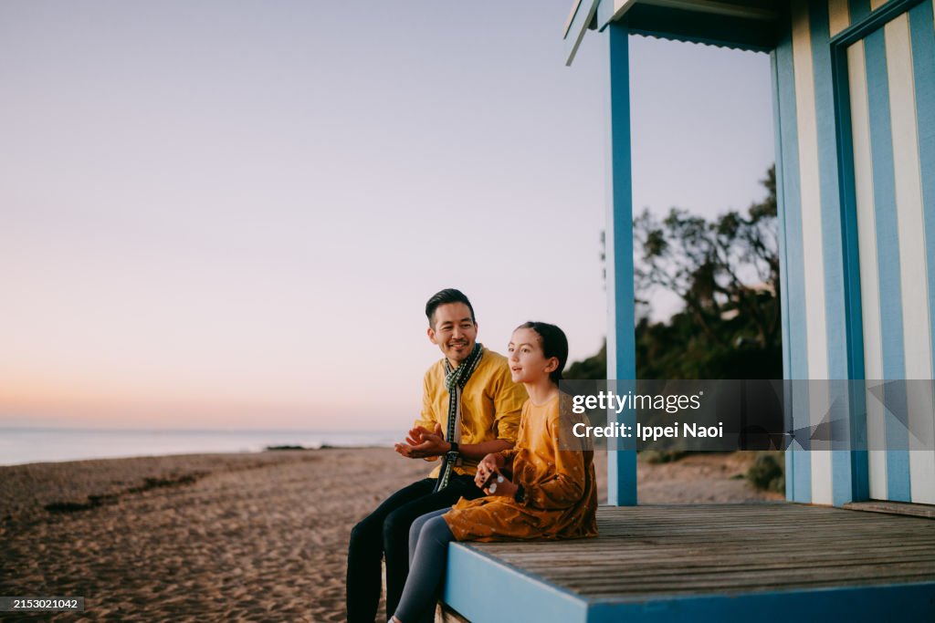 Young girl playing ukulele with her father on beach hut at dusk