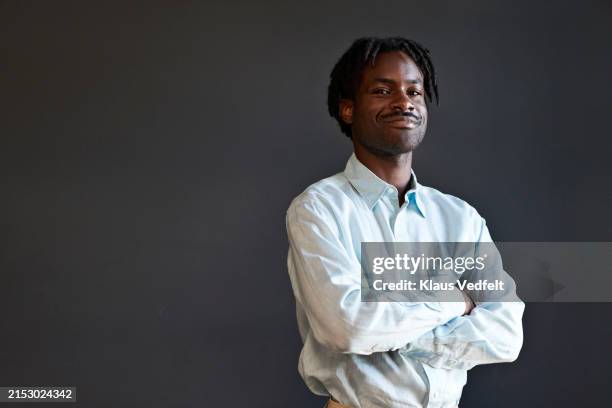 smiling young businessman with arms crossed against black wall - blank shirt stock pictures, royalty-free photos & images