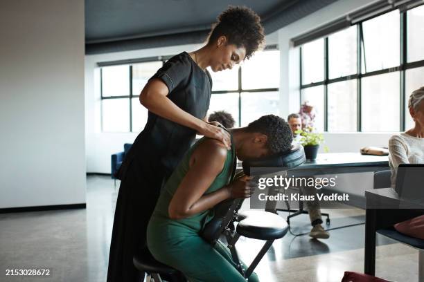 masseuse giving neck massage to tired businesswoman - massagestuhl stock-fotos und bilder
