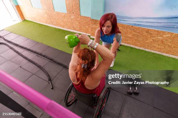 disabled woman exercising with his personal trainer in a gym - paralysis stock pictures, royalty-free photos & images