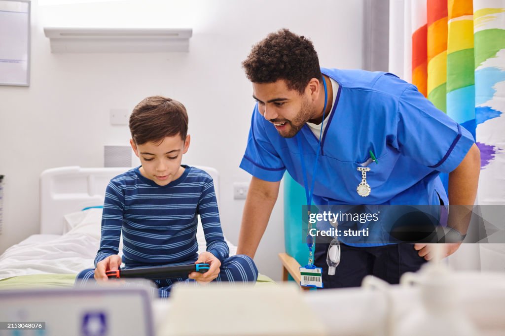 Male pediatric nurse watching child patient playing video game