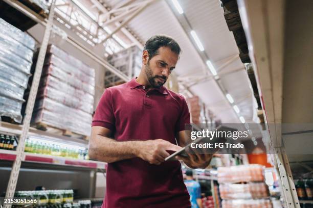 hombre maduro que trabaja en la computadora portátil en el supermercado - vendedor del mercado fotografías e imágenes de stock