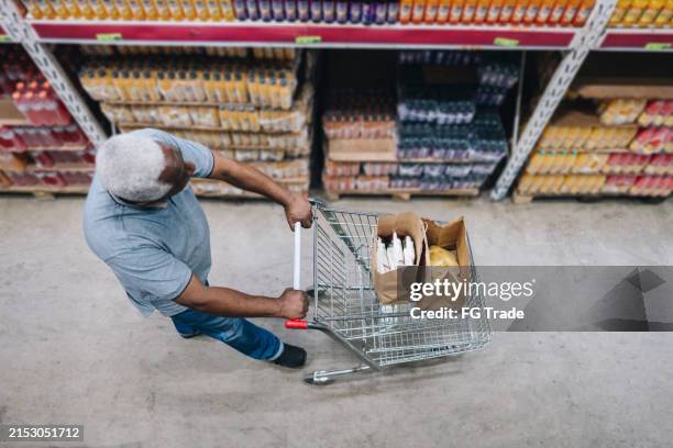 älterer mann geht mit einem einkaufswagen im supermarkt - supermarkt gang stock-fotos und bilder