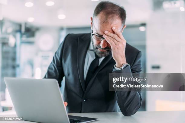 stressed businessman having headache while working on laptop in the office. - disappointment stock pictures, royalty-free photos & images
