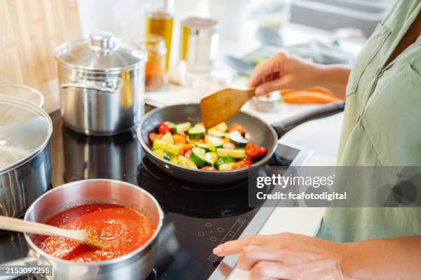 woman adjusting temperature in a stove top while cooks vegetables - keramische plaat stockfoto's en -beelden