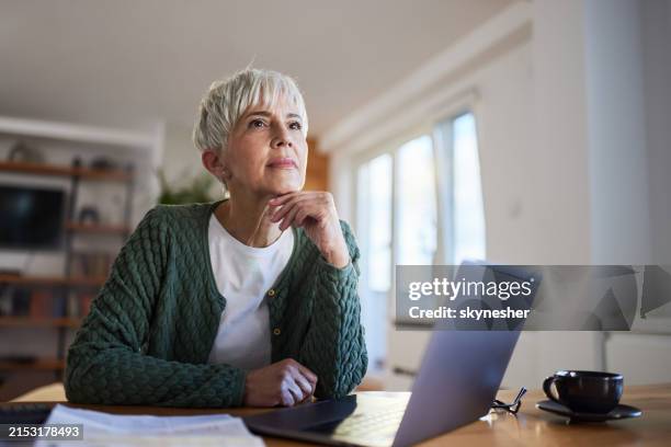 nachdenkliche ältere frau, die zu hause am laptop arbeitet. - nachdenken stock-fotos und bilder