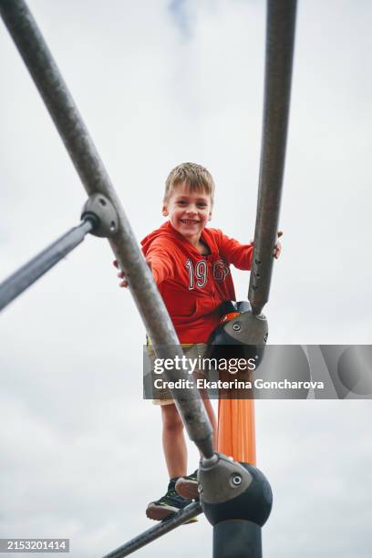 playful smiles at the playground. young boy grasping a bar, cheerful against a backdrop of climbing structures. - klimrek stockfoto's en -beelden