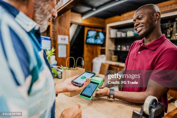verkäufer für mittlere erwachsene, der die zahlung mit smartphone über nfc im blumenladen erhält - markt verkaufsstätte stock-fotos und bilder