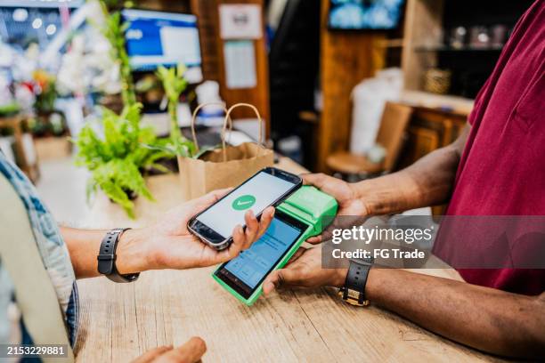 close-up of a customer paying with smartphone using nfc at flower shop - markt verkaufsstätte stock-fotos und bilder