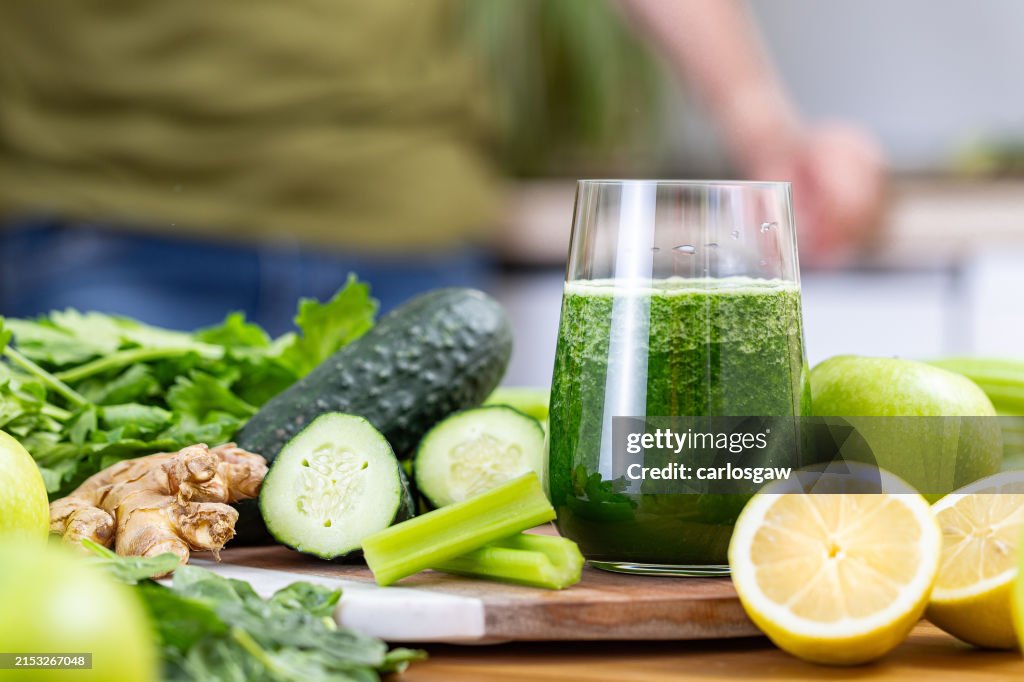 Glass of detox juice surrounded by fruits and vegetables on a kitchen table