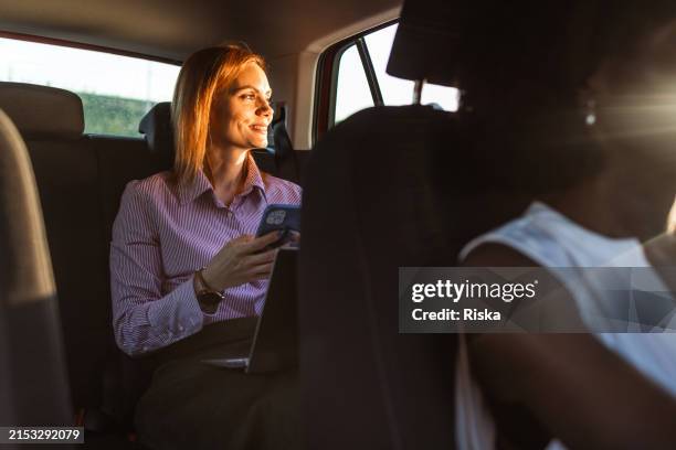 femme d’affaires d’âge moyen utilisant un téléphone intelligent et un ordinateur portable pendant un trajet en voiture - seulement des femmes dâge moyen photos et images de collection