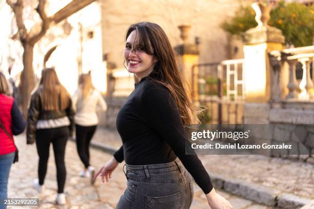 woman turning to smile at camera while walking along the street - regarder par dessus son épaule photos et images de collection
