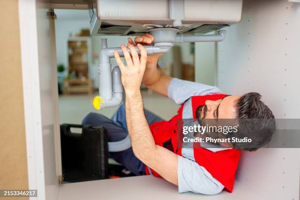 a plumber carefully fixes a leak in a sink - kitchen sink stock pictures, royalty-free photos & images
