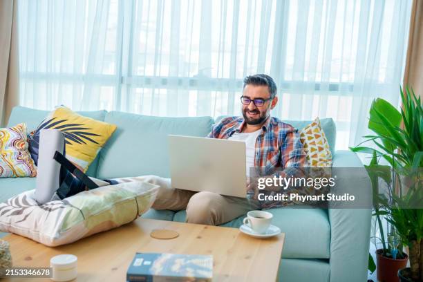 un hombre de negocios de unos 40 años, que trabaja desde casa, estira su pie roto sobre una almohada colocada sobre la mesa de café. - muleta fotografías e imágenes de stock