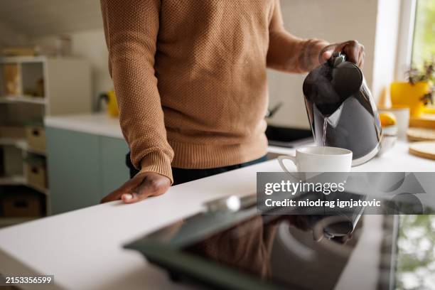 young man using an electric kettle to make tea at home - kettle stock pictures, royalty-free photos & images